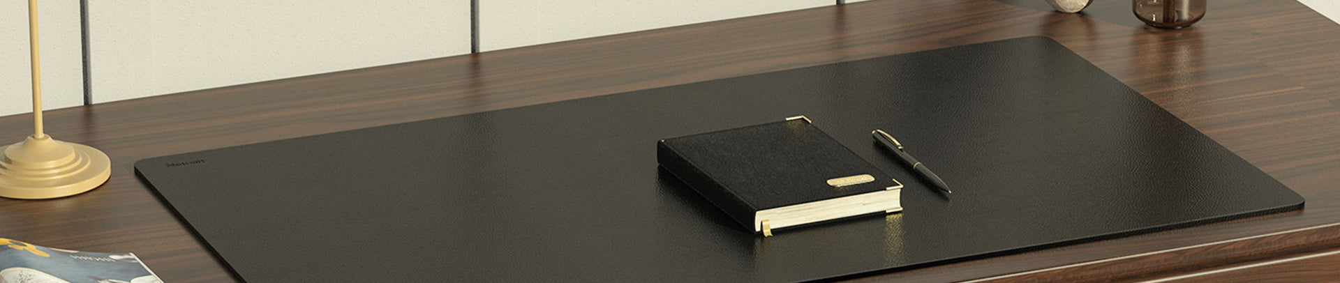 Black desk mat with a notebook and pen on a wooden desk