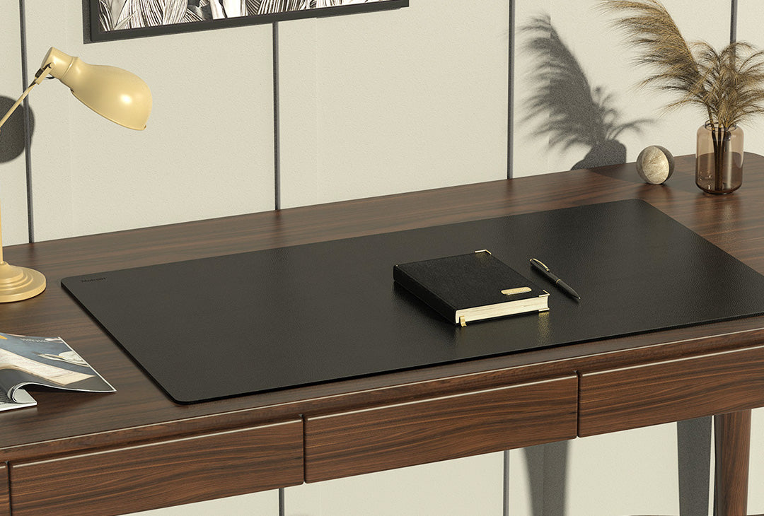 Wooden desk with black desk pad, notebook, and pen in a home office setting.