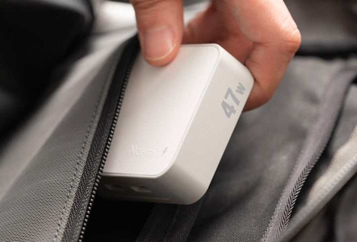 Hand holding a white power bank with '47W' branding against a gray fabric background