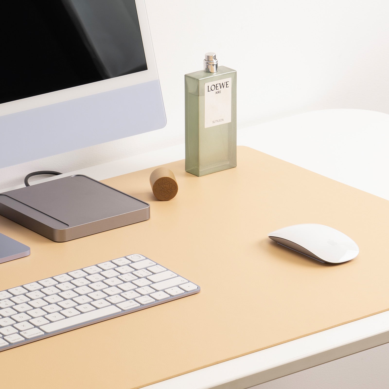 Desk setup with computer monitor, keyboard, mouse, and a Loewe bottle on a beige desk.