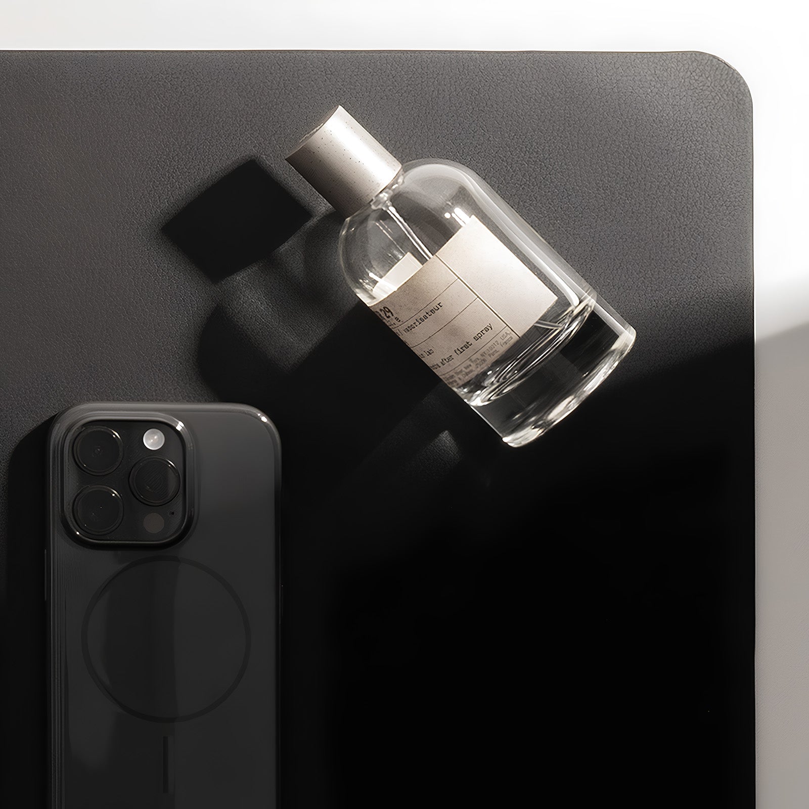 Clear glass bottle with silver cap on a dark surface next to a smartphone