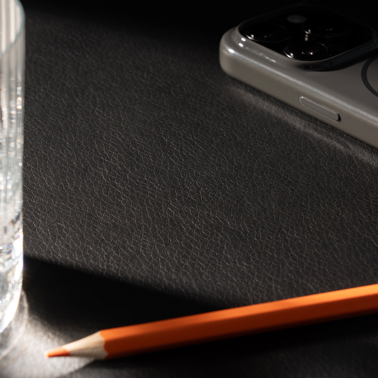Orange pencil on a black leather surface with a smartphone in the corner.