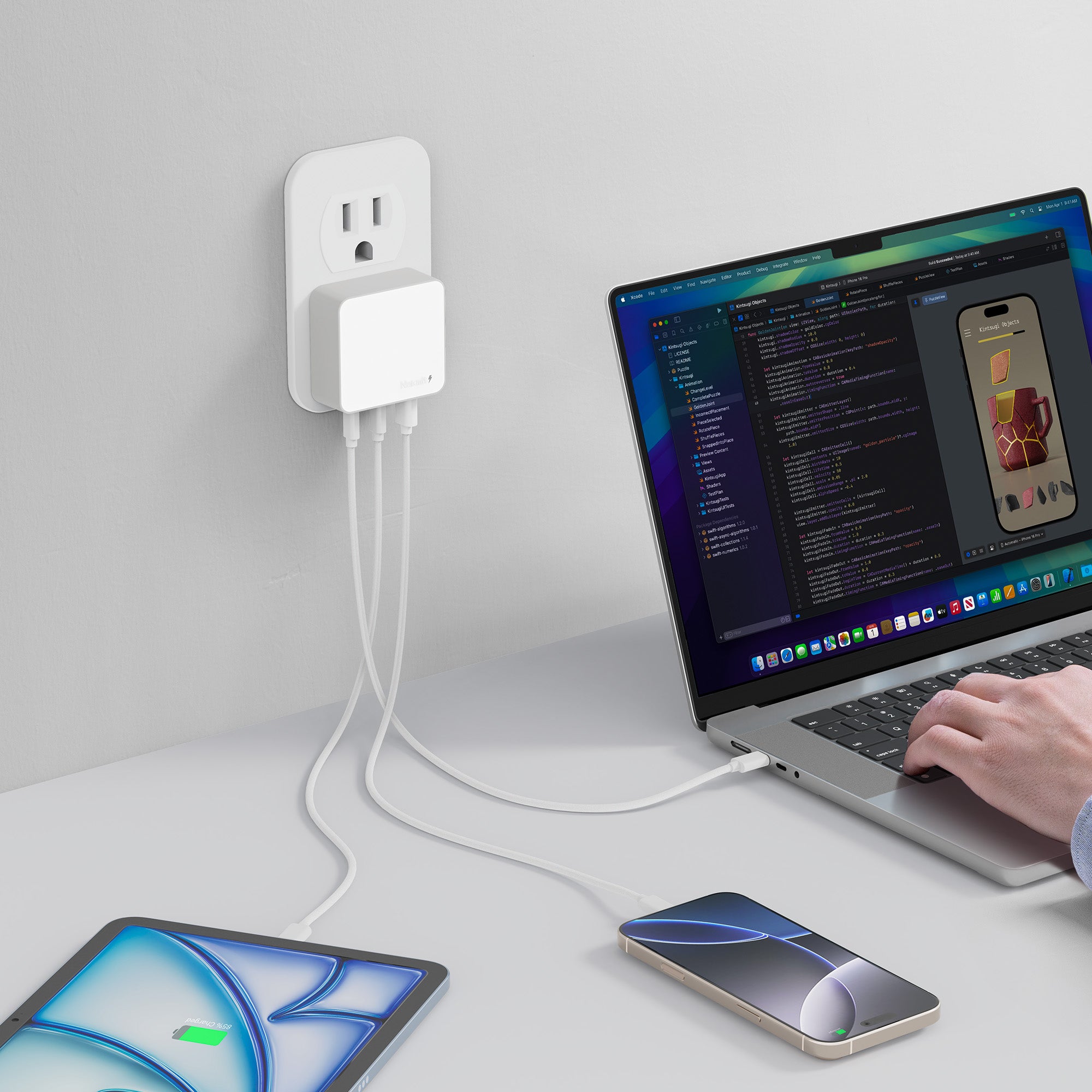 Person using a laptop with multiple devices connected to a power adapter on a white desk.