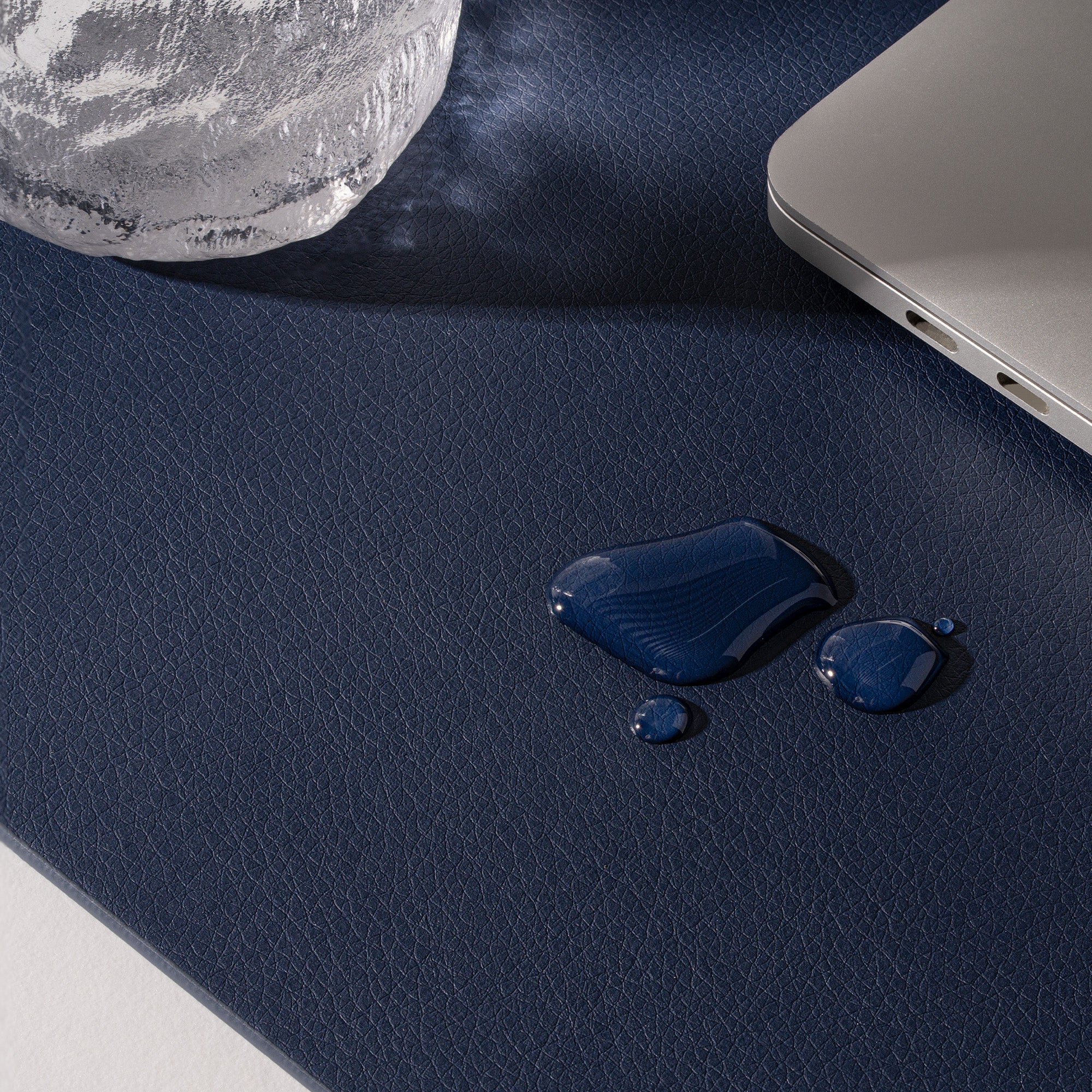 Blue liquid spill on a dark blue surface with a laptop and spherical object in the background.