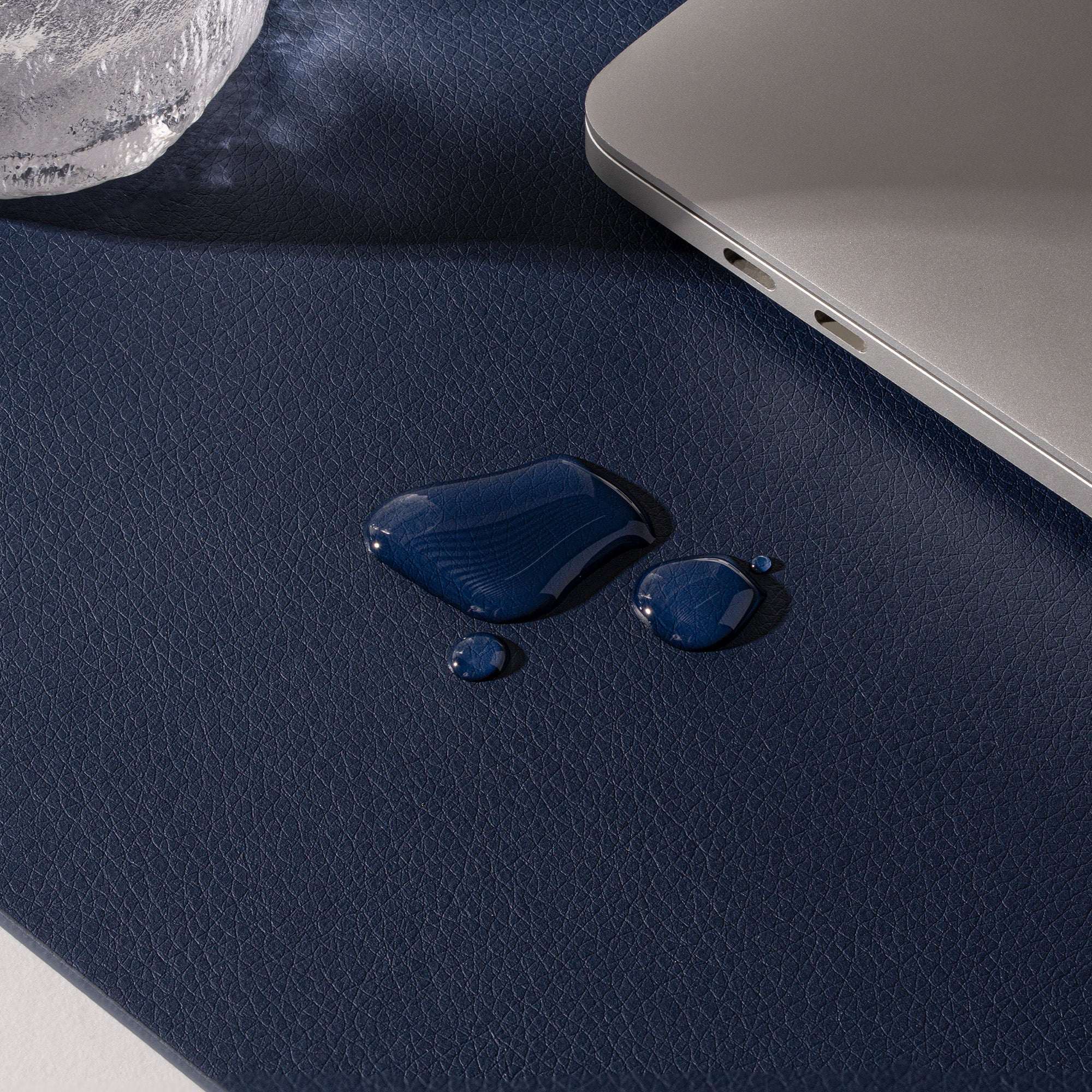 Blue liquid droplets on a dark blue surface with a laptop corner visible