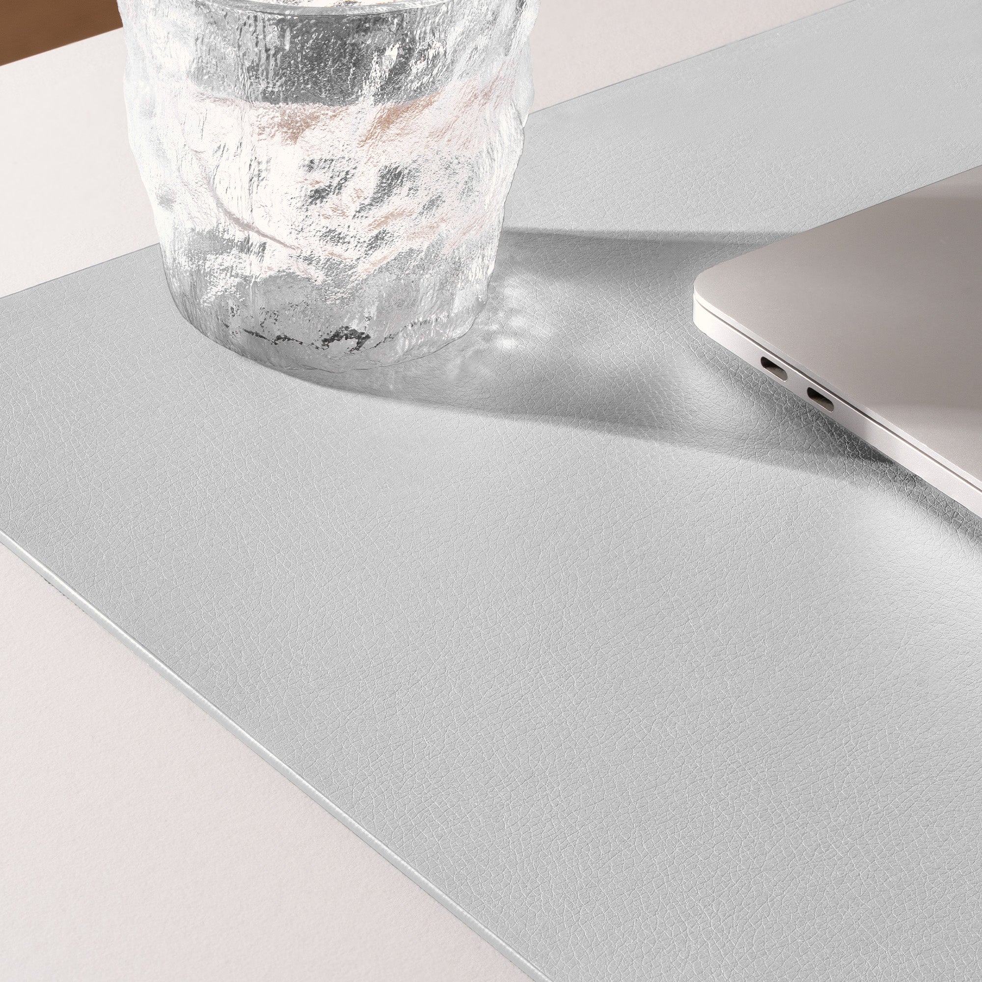 Gray desk mat with a glass and laptop on a light surface