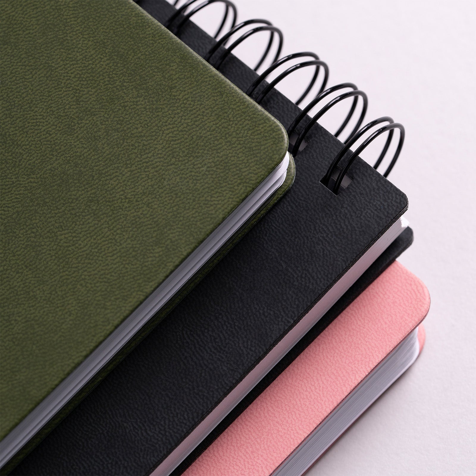 Stack of three notebooks in green, black, and pink on a light gray background