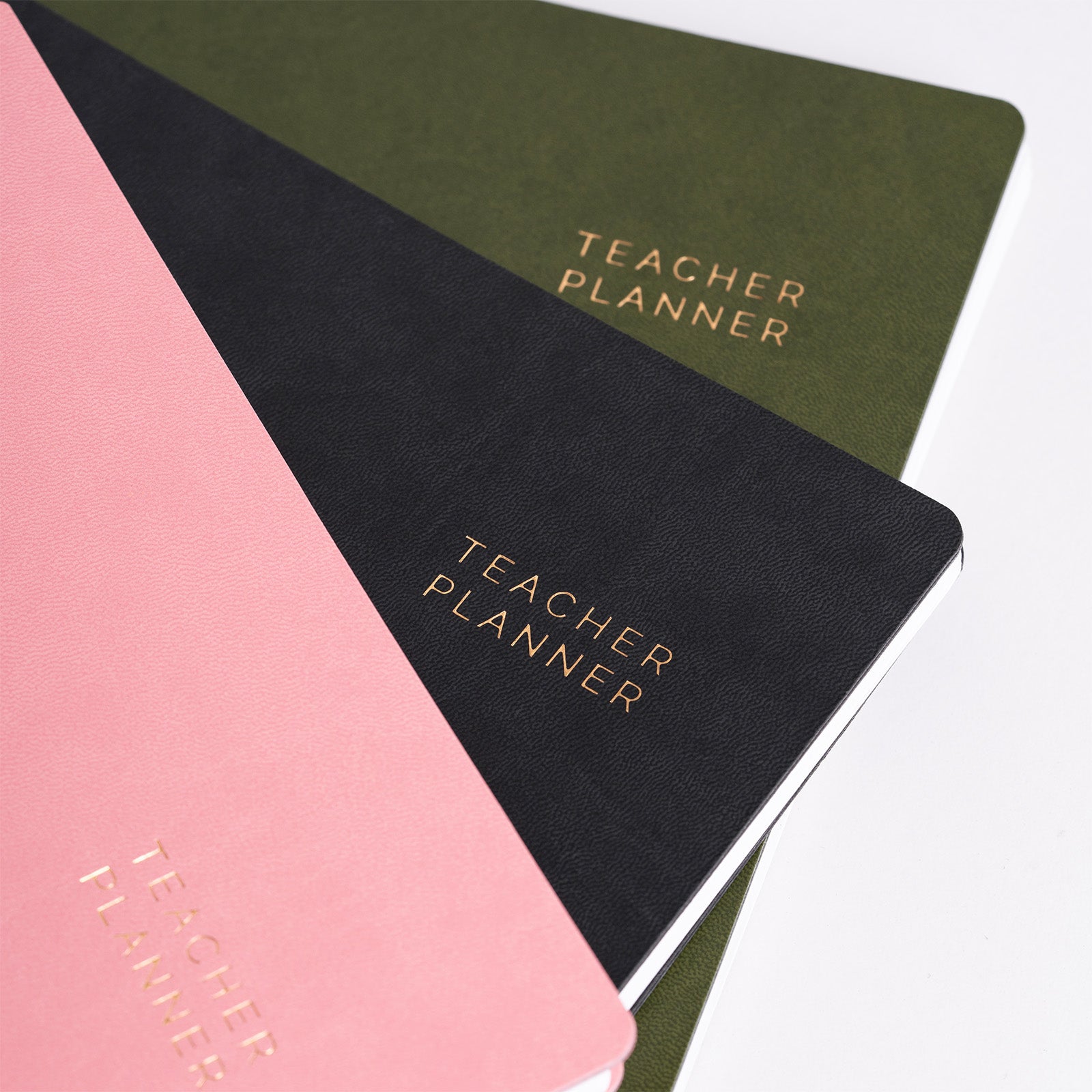 Four teacher planners in different colors including pink, green, black, and beige on a white background.