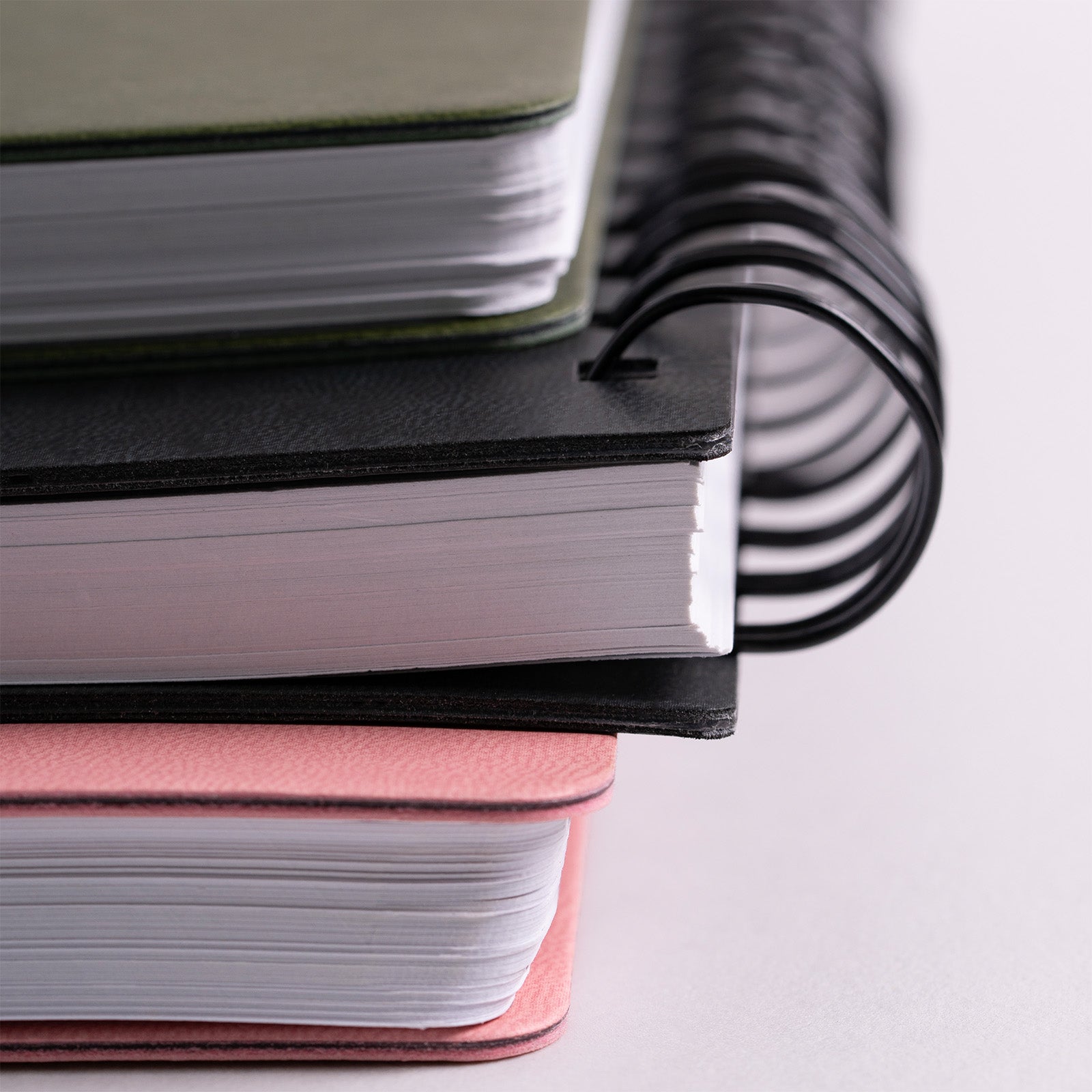 Stack of notebooks with black, green, and pink covers on a light gray background