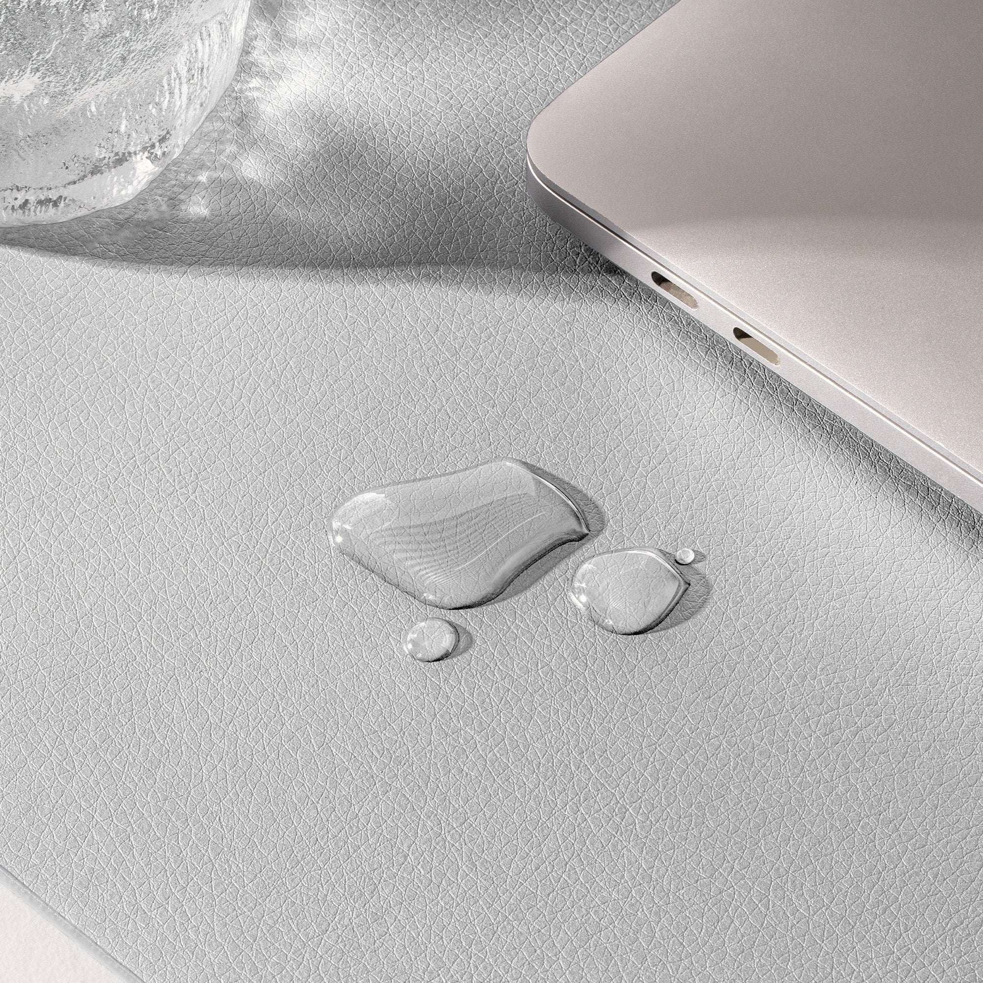 Close-up of a textured surface with water droplets and a laptop corner.