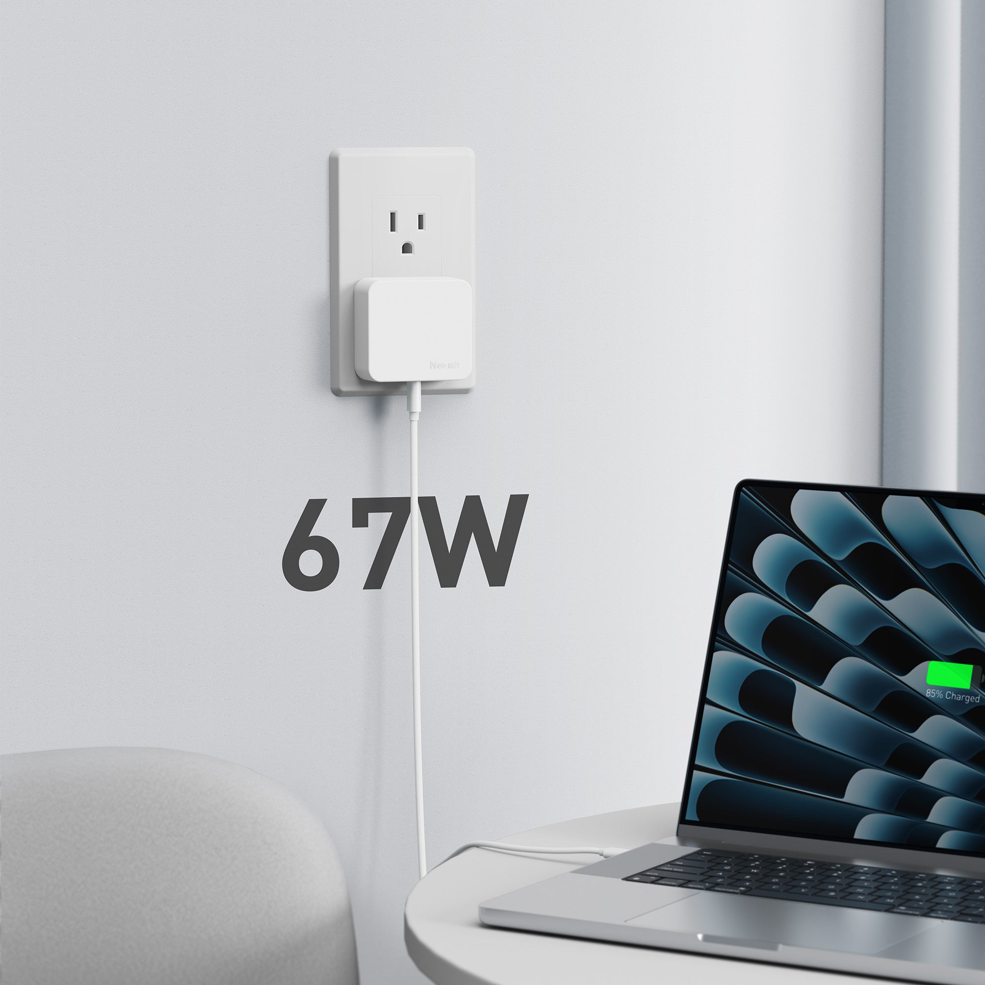 Laptop connected to a power adapter with '67W' displayed on a white wall.