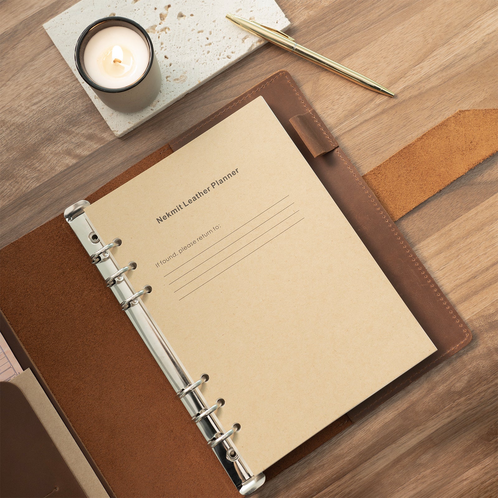 Brown leather planner with beige cover on a wooden surface with a candle and pen.