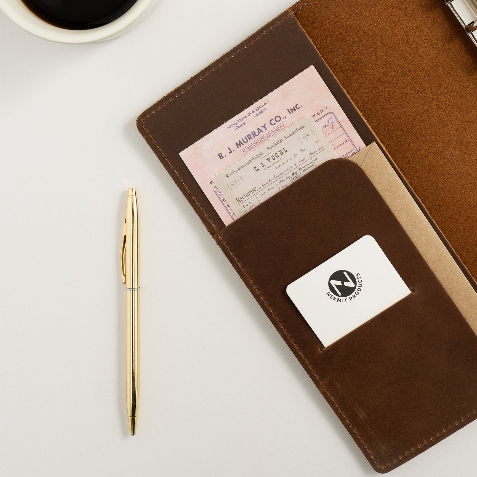 Brown leather wallet with card and check, gold pen, and coffee cup on a light gray background