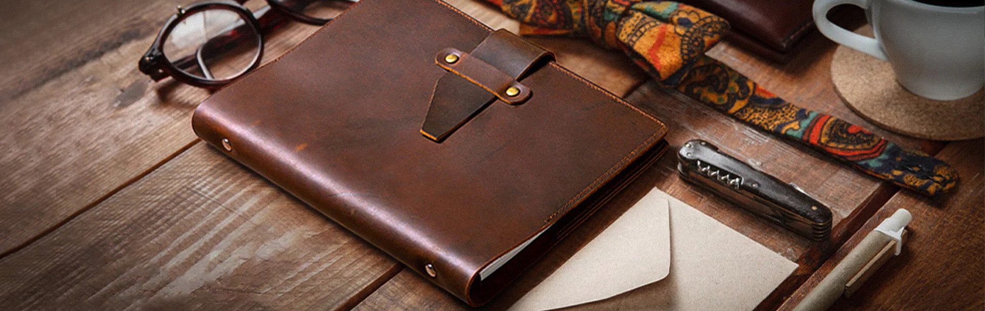 Brown leather notebook on a wooden surface with a tattooed arm and coffee cup in the background