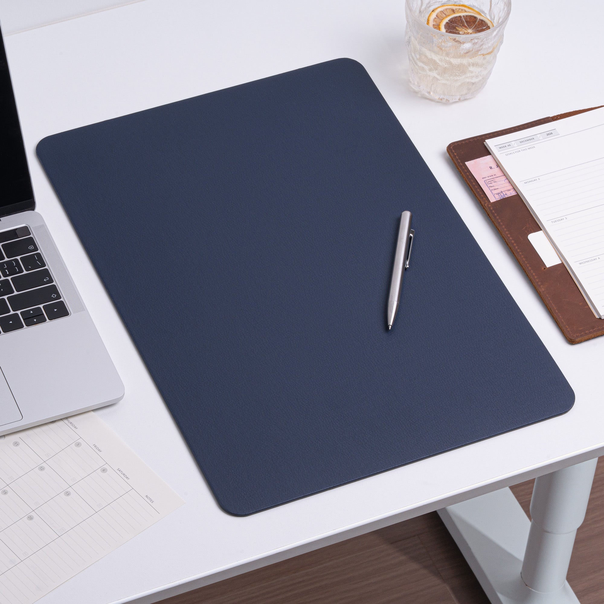 Dark blue desk pad on a white desk with a pen, laptop, and notebook.