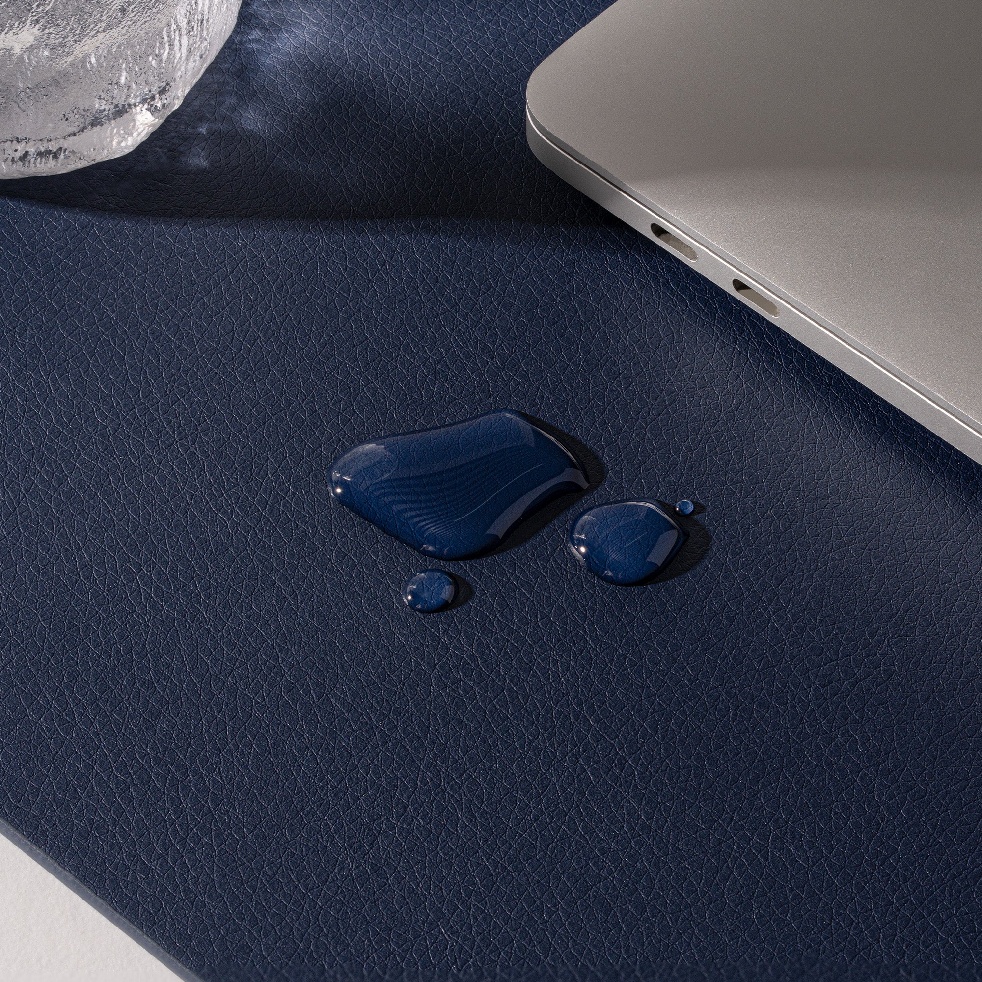 Blue liquid droplets on a dark blue surface with a laptop corner visible