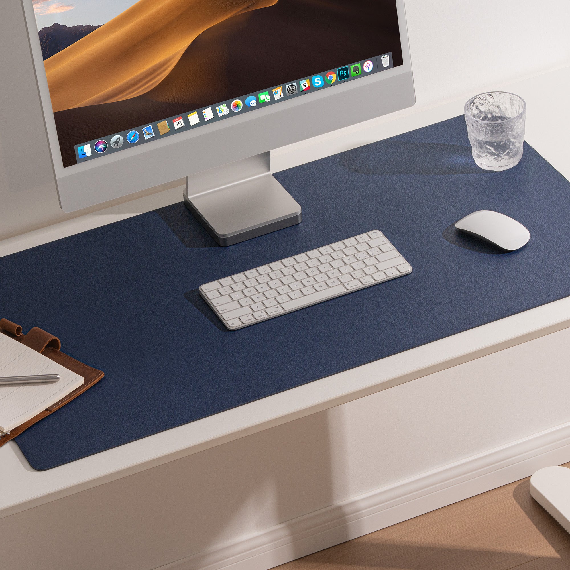 Modern office desk setup with a computer monitor, keyboard, mouse, and glass on a blue desk pad.