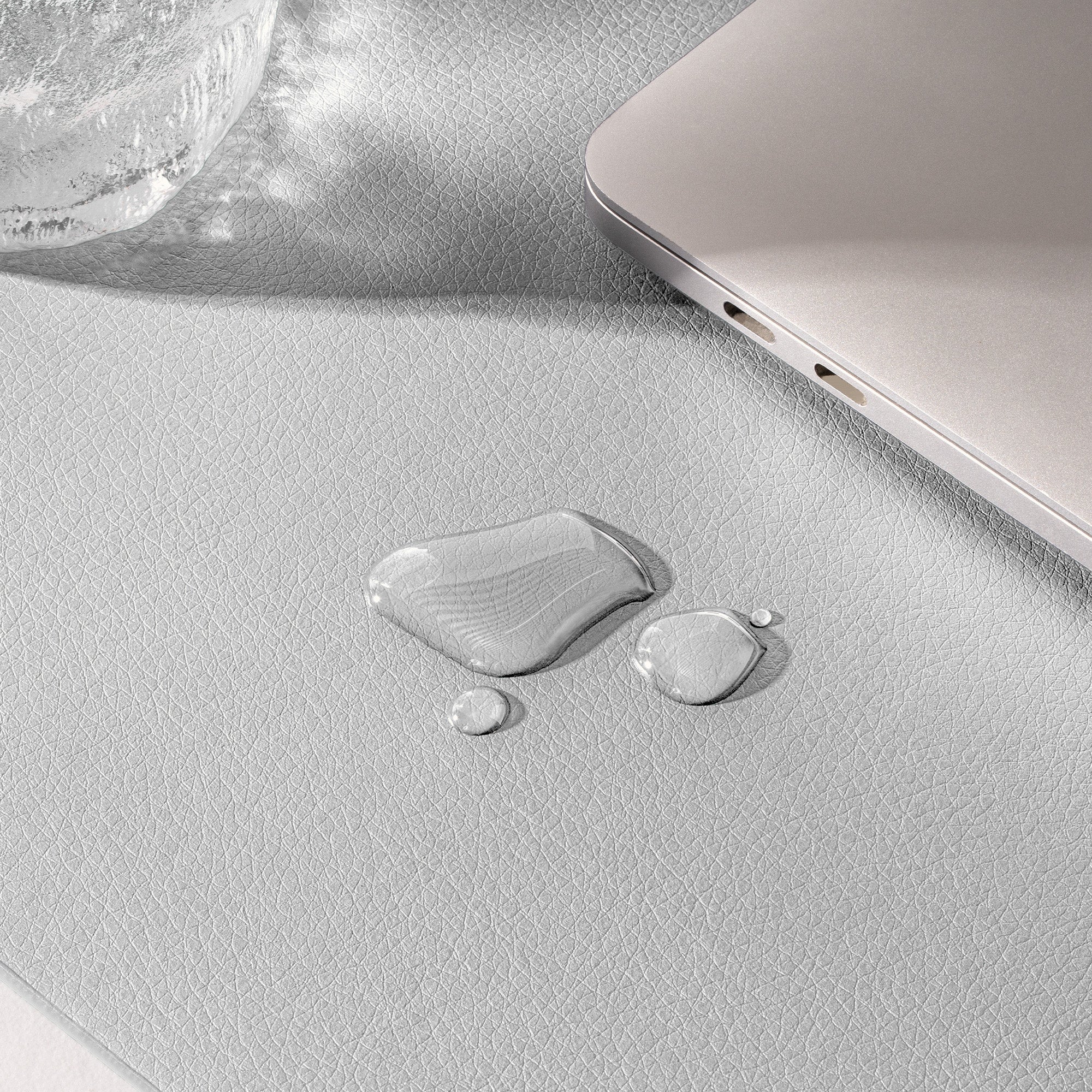 Close-up of a textured surface with water droplets and a laptop corner.