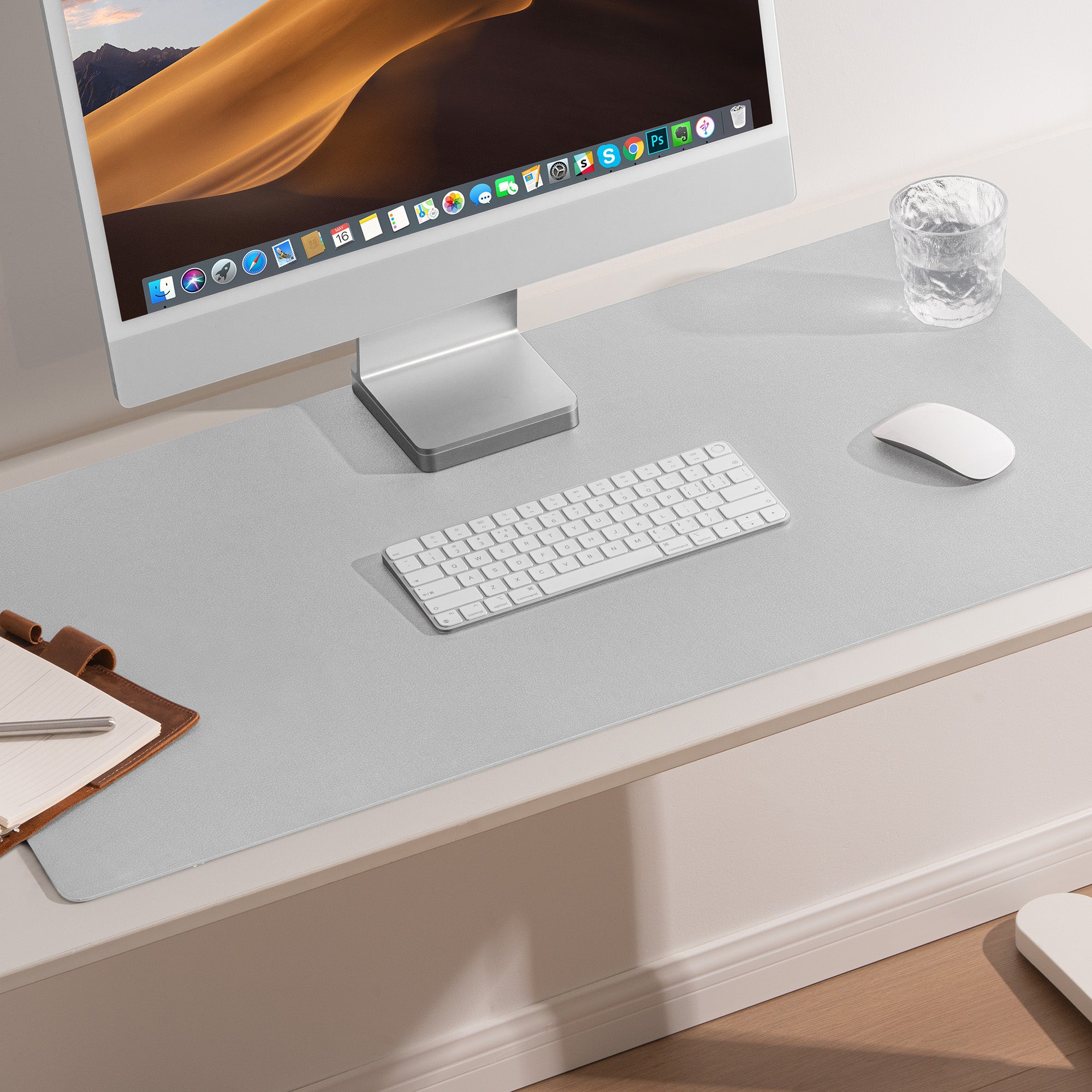 Modern office desk setup with computer monitor, keyboard, mouse, and glass on a light gray desk.