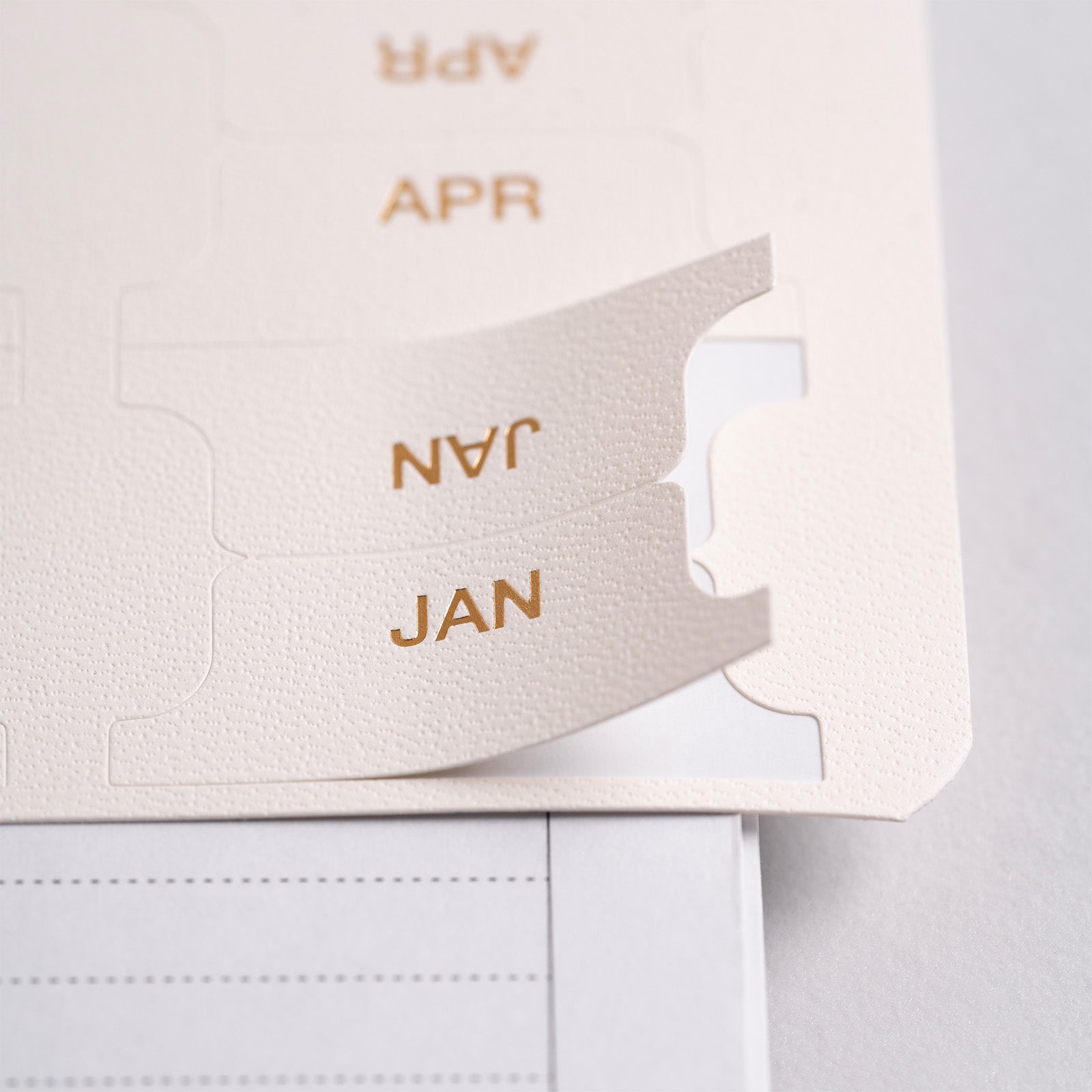 Close-up of a beige planner with 'JAN' and 'APR' text on a light gray background