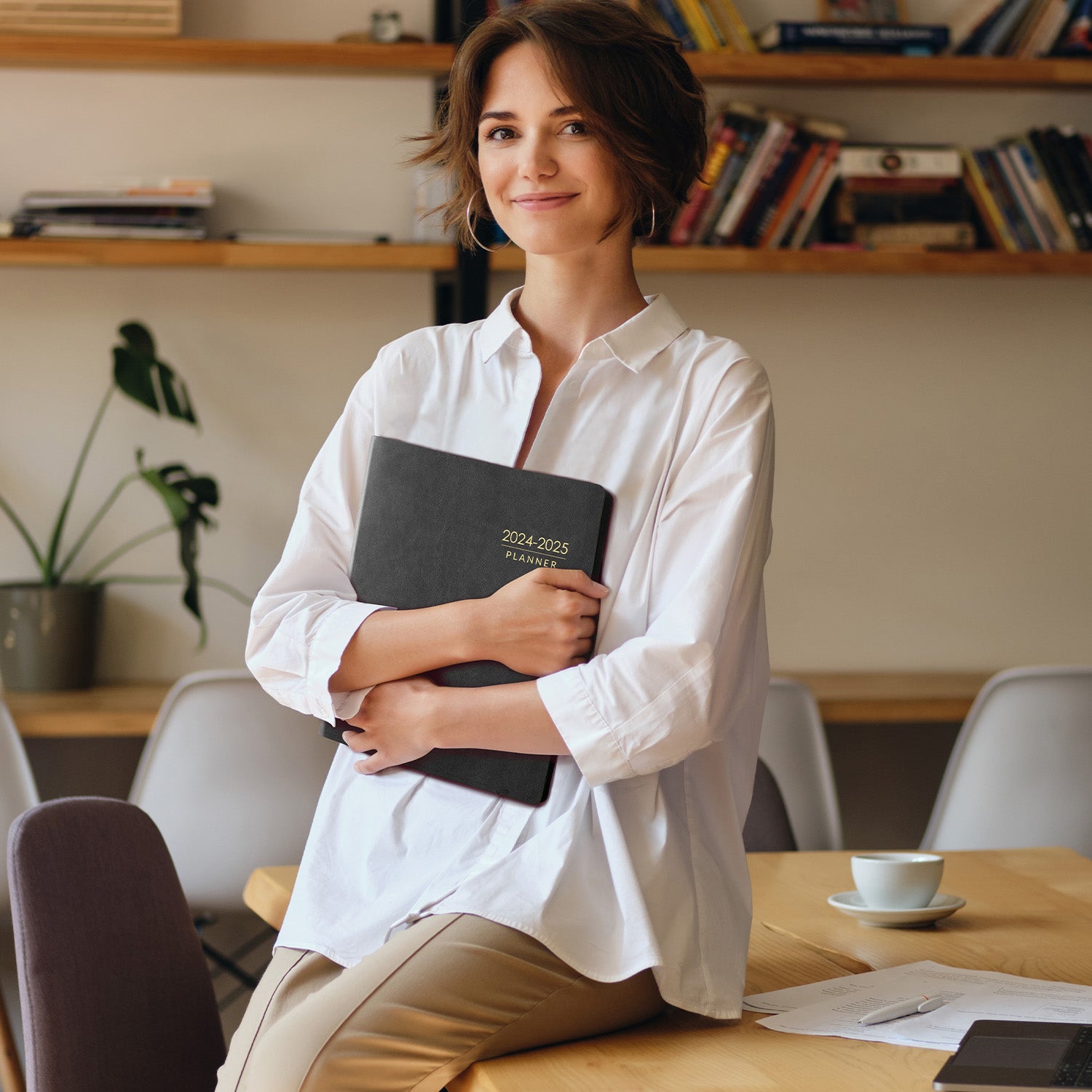 Woman holding a planner in an office setting with books and a plant in the background
