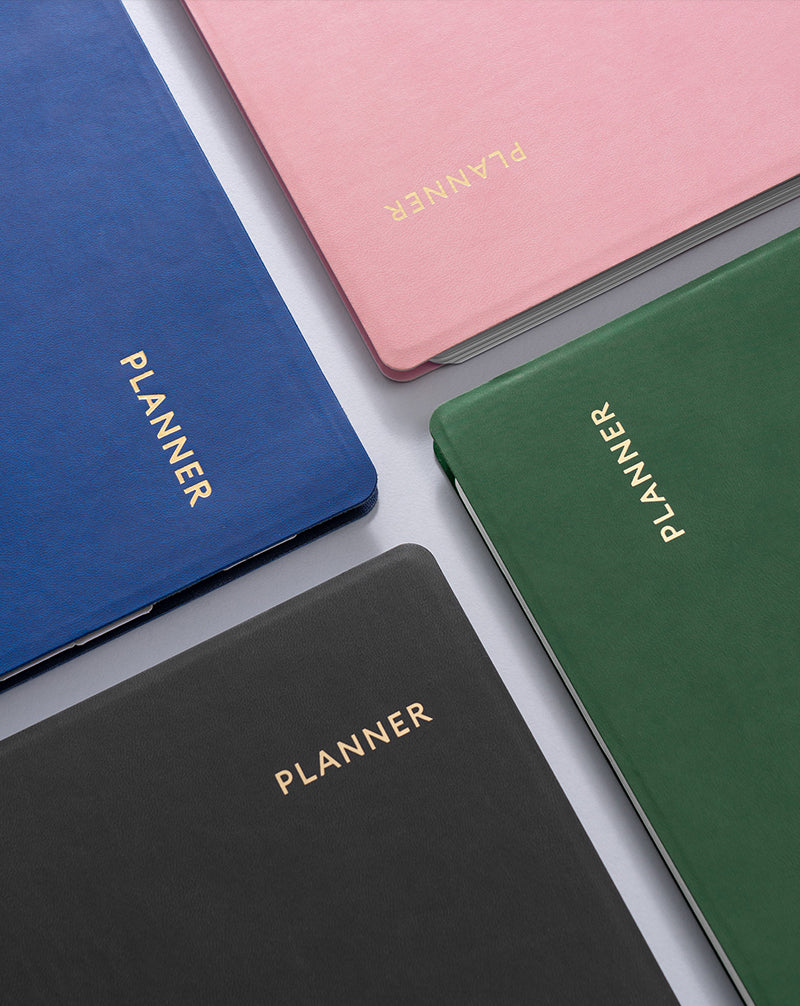 Four planners in blue, pink, green, and black with 'PLANNER' text on a light gray background.